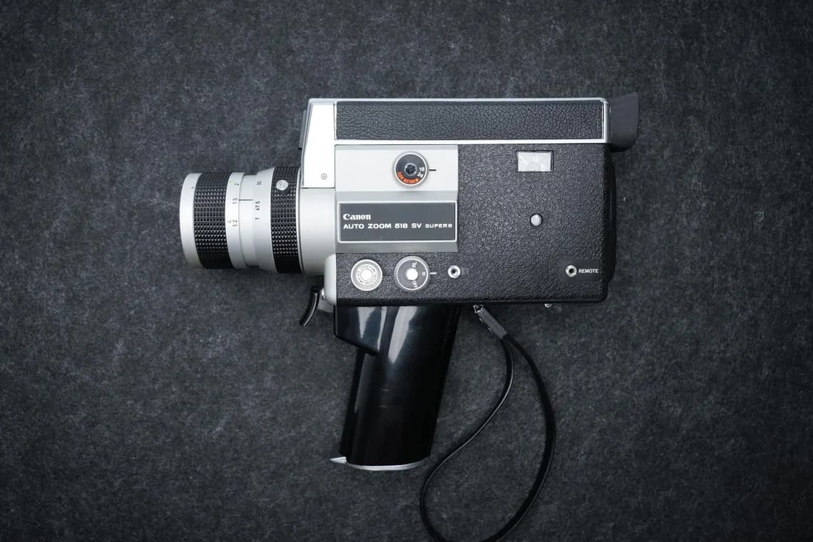 A black and silver Canon Auto Zoom 518 SV Super 8 movie camera with a pistol-grip handle and zoom lens, photographed from above on a dark grey surface.